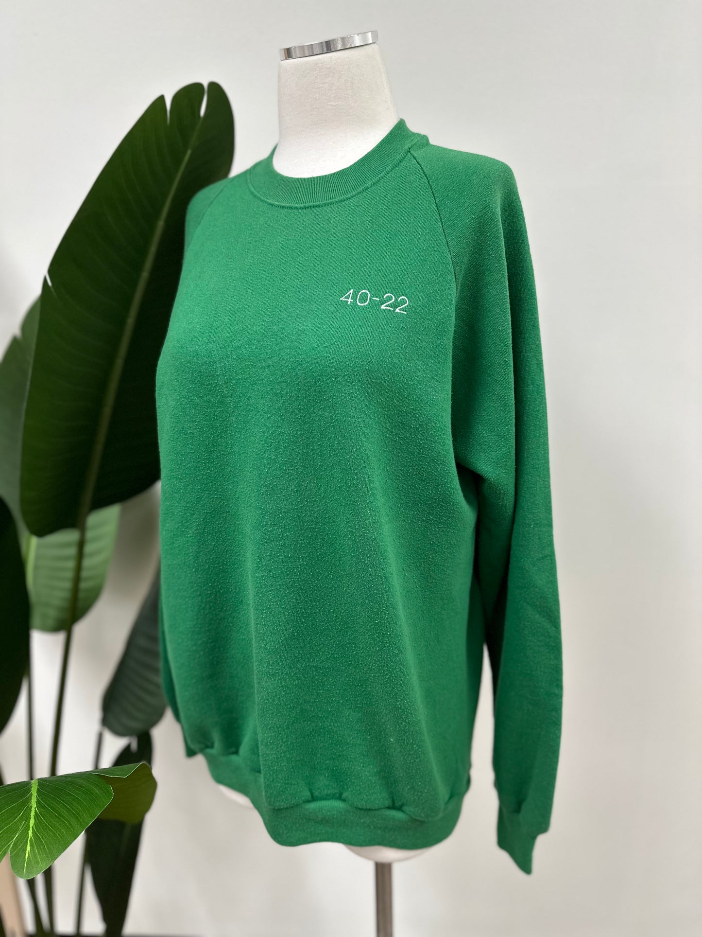 Side view of a kelly green vintage crewneck with a white embroidered Super Bowl Score