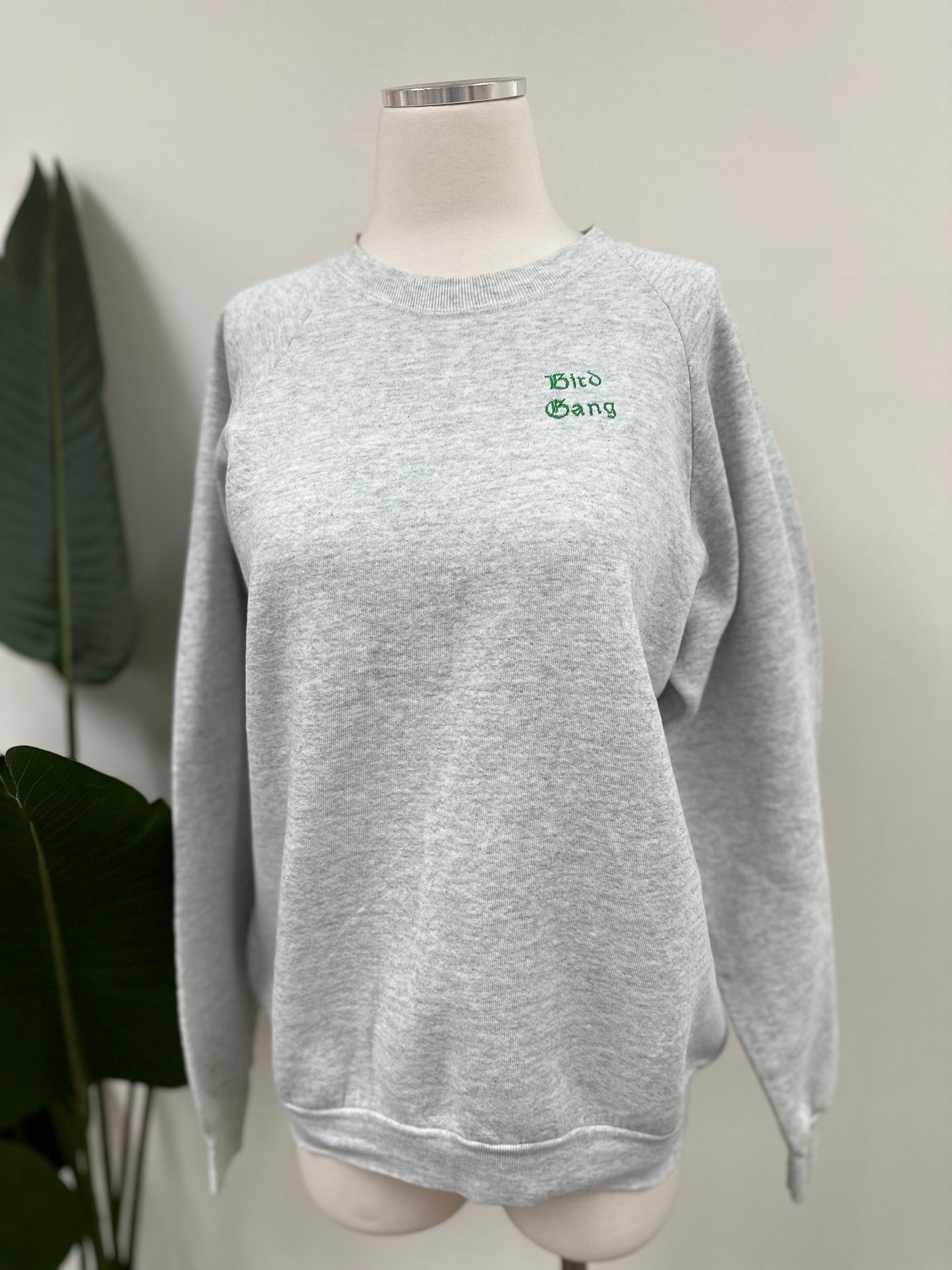 Front view of a heather grey vintage crewneck with green bird gang embroidery