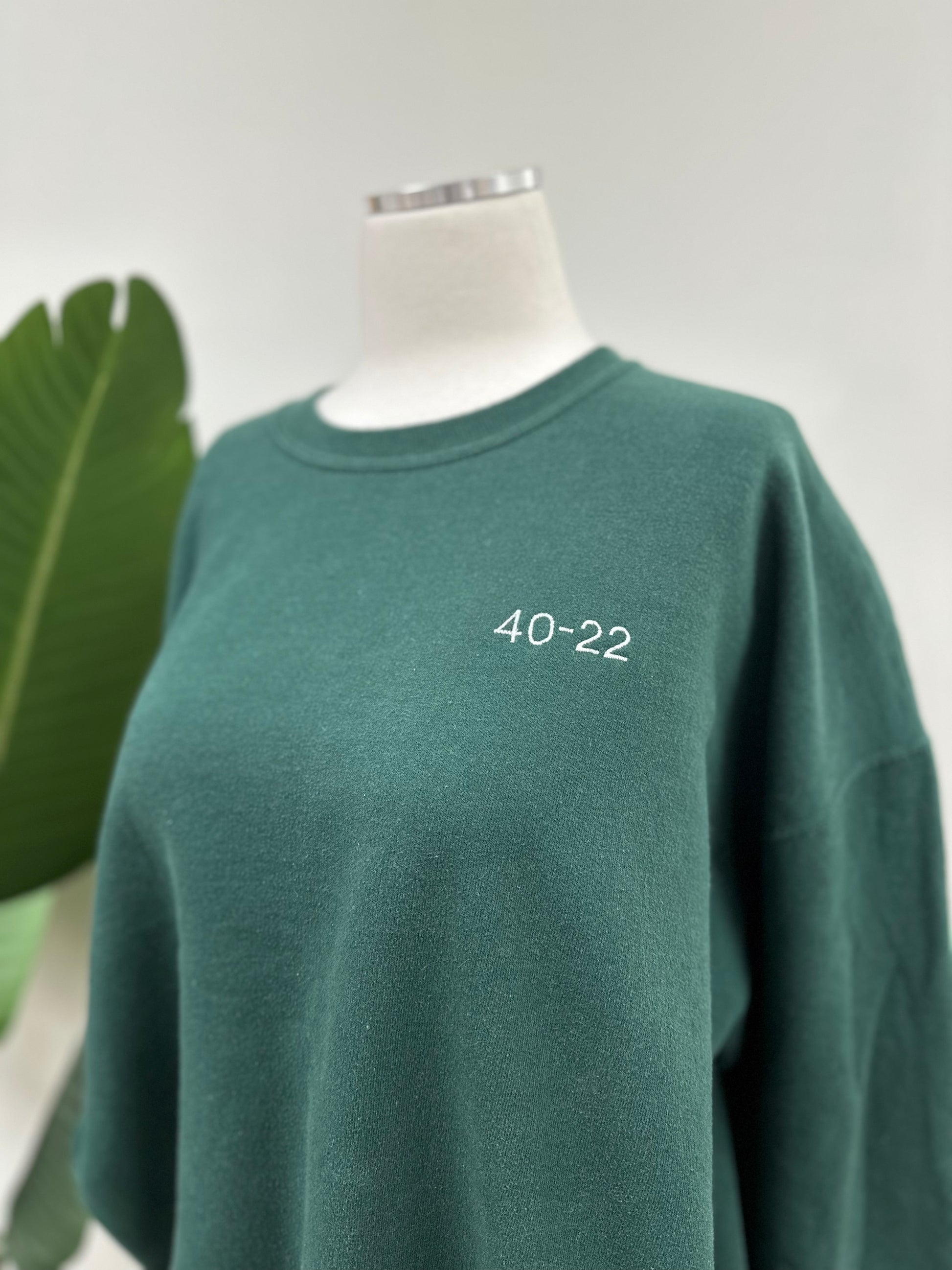 Close up view of a green vintage crewneck with a white embroidered Super Bowl Score