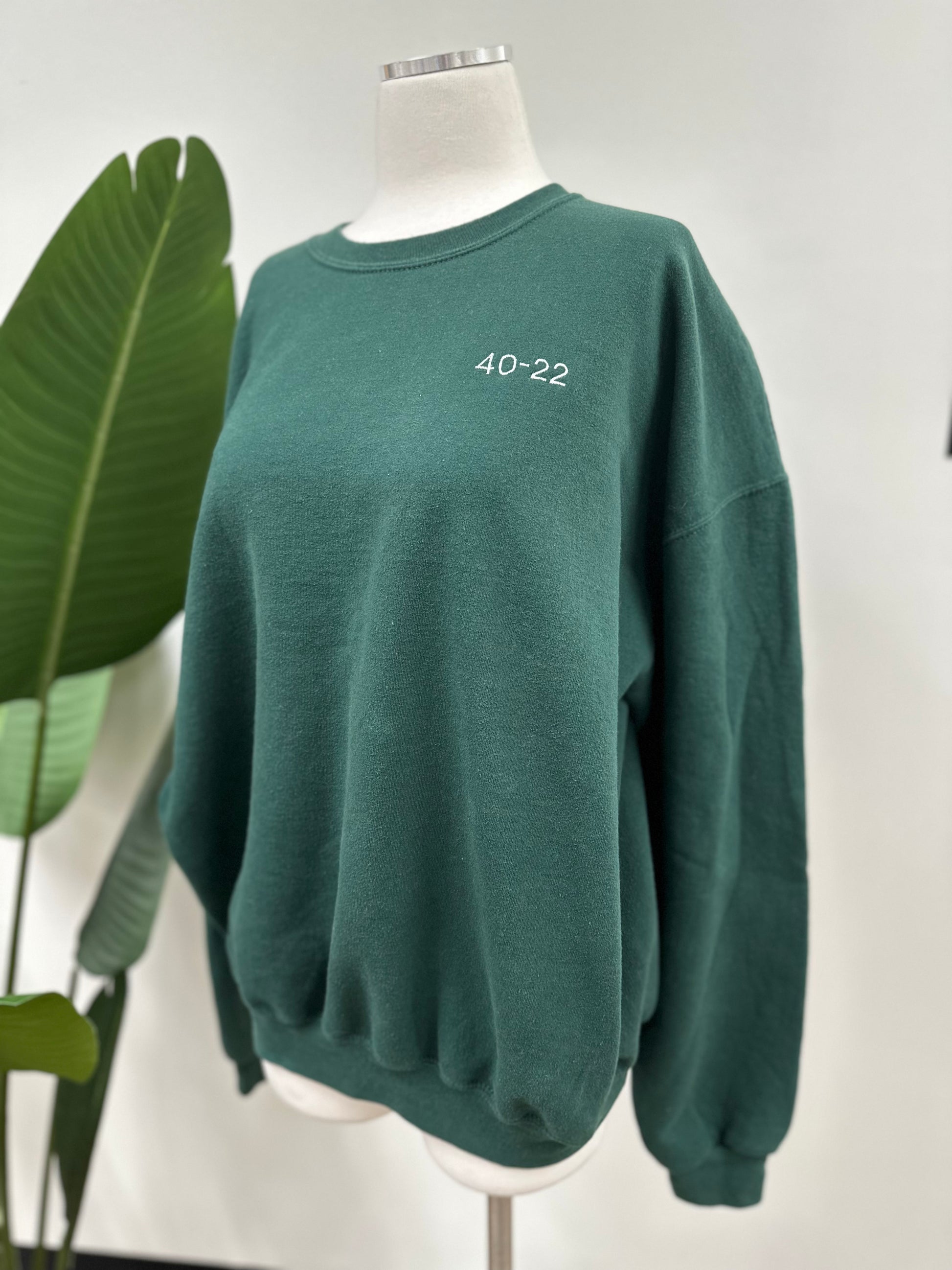 Side view of a green vintage crewneck with a white embroidered Super Bowl Score