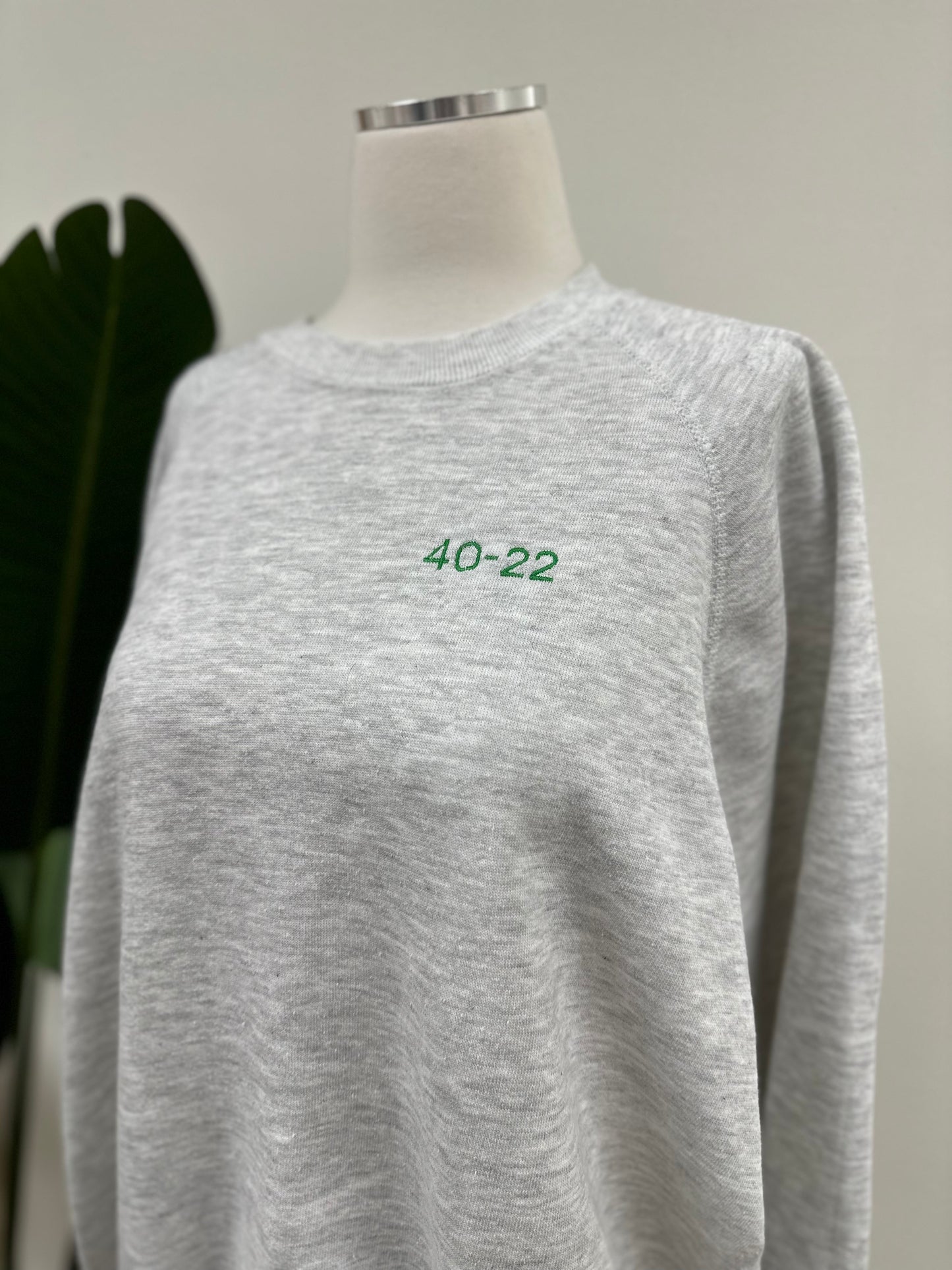 Close up view of a heather grey vintage crewneck with a green embroidered Super Bowl Score