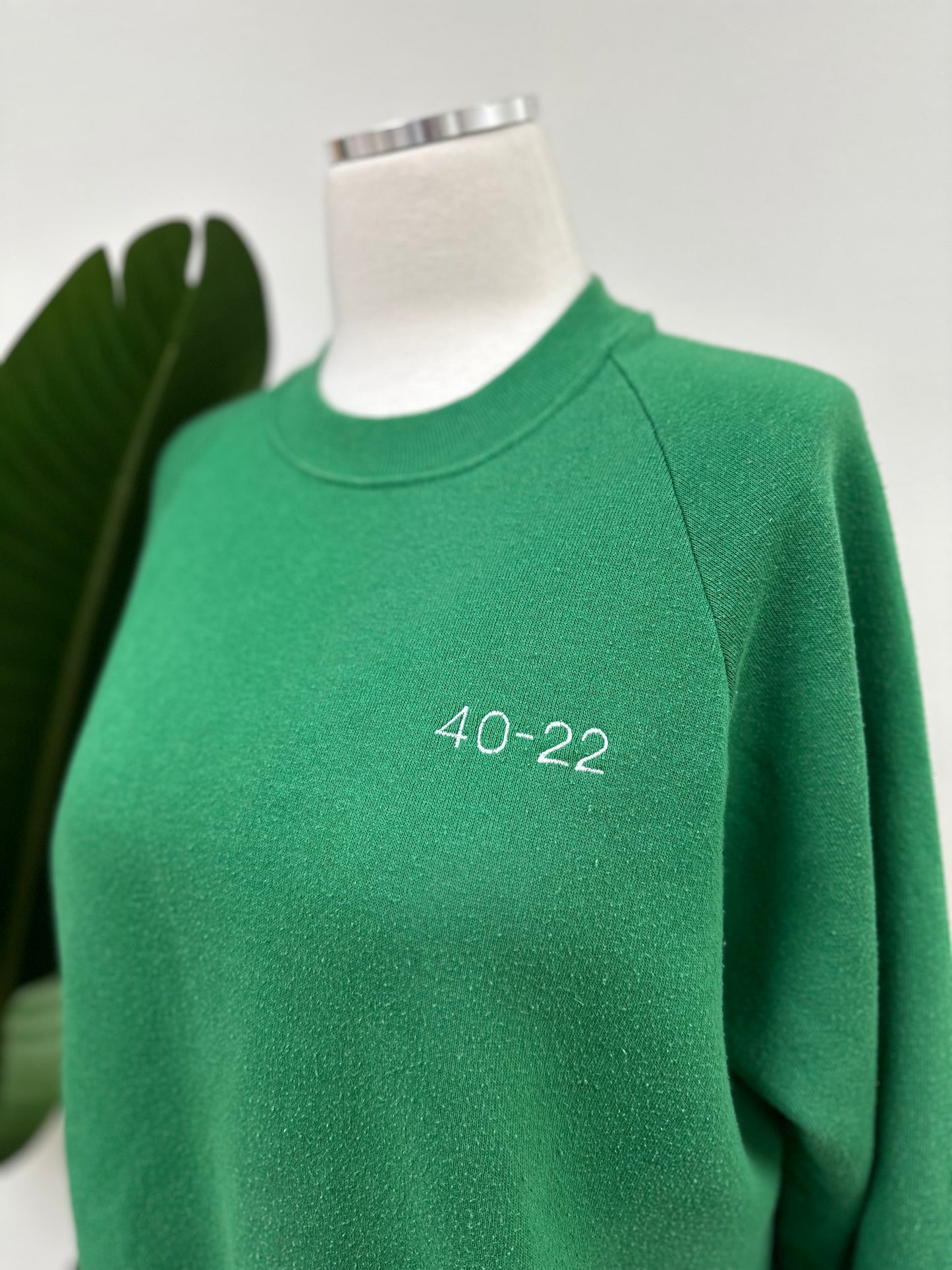 Close up view of a kelly green vintage crewneck with a white embroidered Super Bowl Score