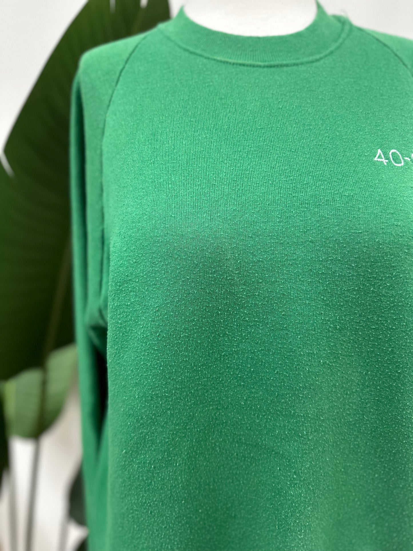 Detail shot of minor discoloration on a kelly green vintage crewneck with a white embroidered Super Bowl Score